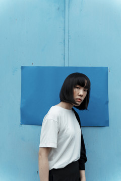 年轻的泰国亚裔女子，深色短发，蓝色背景，在街上。实体模型。纸张模板。
