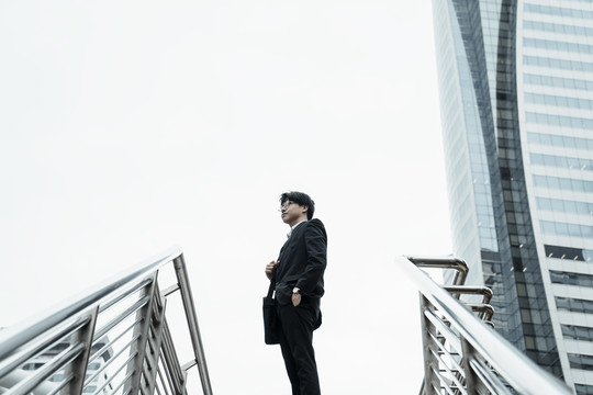 穿着黑色西装的年轻亚洲商人站在城市里——复制空间。