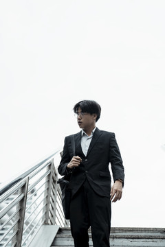 年轻的亚洲商人穿着黑色西装走下楼梯在这个城市。