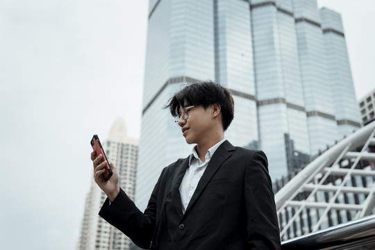 在曼谷市街头，年轻的亚洲商人在户外使用智能手机工作。