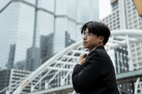 身穿黑色西装戴眼镜的亚洲帅哥商人站在城市背景上-复印空间