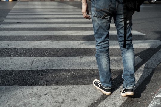 牛仔裤牛仔腿上的亚洲旅游背包客走过马路。