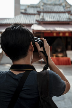 年轻英俊的亚洲摄影师在中国文化庙里用相机拍照。