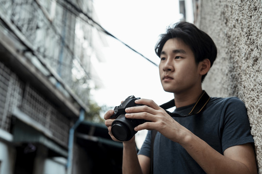 年轻英俊的亚洲摄影师手持相机走在街上。街头摄影。