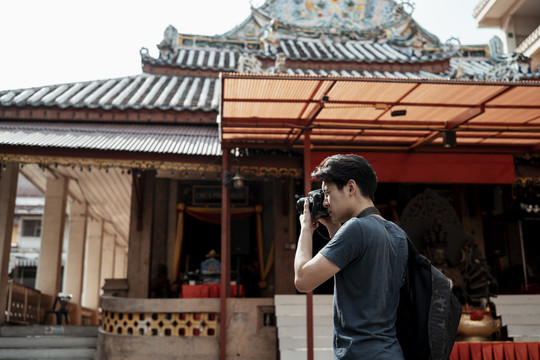 年轻英俊的亚洲摄影师在中国寺庙里用相机拍照。