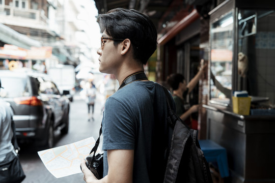 年轻英俊的亚洲摄影师戴着墨镜拿着地图走在曼谷街头。