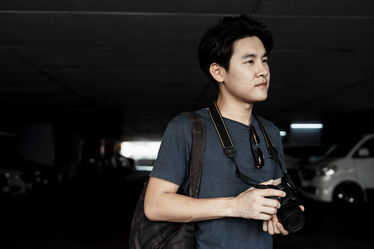 年轻英俊的亚洲摄影师手持相机站在