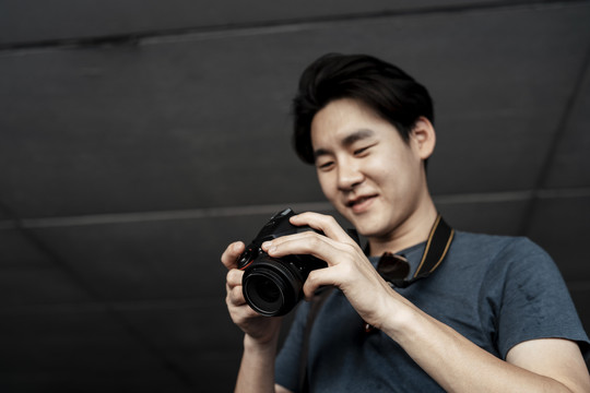 年轻英俊的亚洲摄影师满足于相机里的照片。