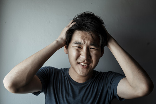 人类的面部表情-紧张的亚洲男人用双手捂着头，担心，烦恼，悲伤，不开心。头痛和偏头痛。