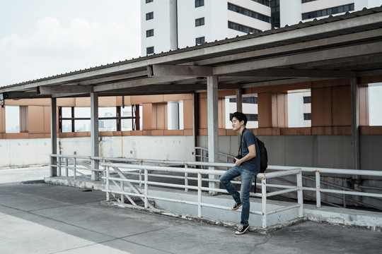 年轻英俊的亚洲摄影师坐在屋顶上。城市街头摄影。