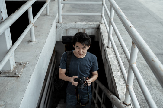 年轻英俊的亚洲摄影师走在废弃建筑的楼梯上。