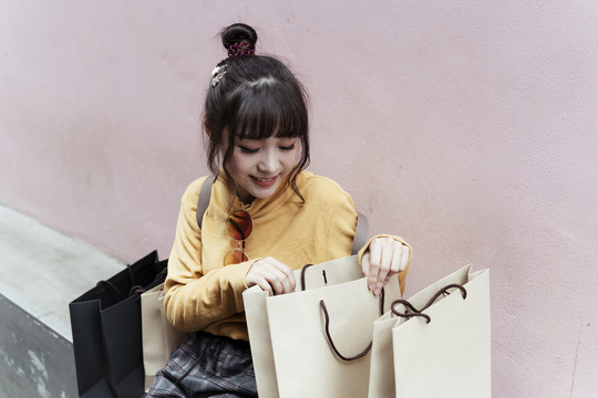 一位亚洲妇女在粉红色背景下看着购物纸袋里的东西。