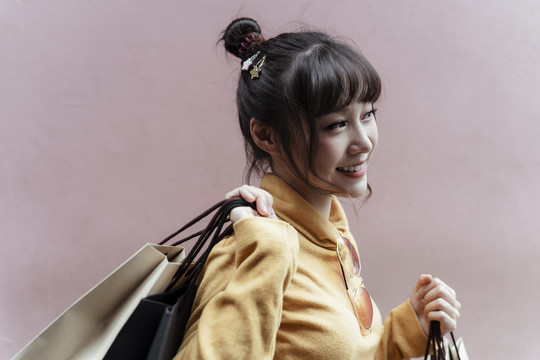 穿着黄色毛衣站在粉色背景上的快乐的亚洲年轻女子。