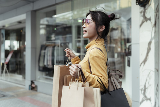 时尚达人快活的亚洲女人喜欢穿着黄色毛衣戴着时尚眼镜在商店外的大街上逛街。