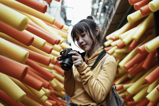 一位身穿黄色毛衣的亚洲年轻女子手持相机在街巷的嘉年华活动中拍照。