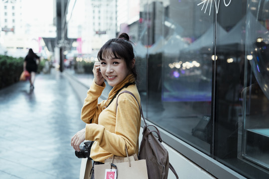 美丽的亚洲可爱女人穿着黄色毛衣拿着购物纸袋看着街上的相机。