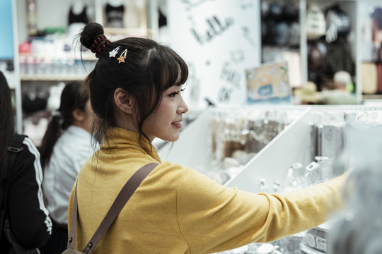 穿着黄色衬衫的漂亮女孩在商店的白色文具前寻找商品。