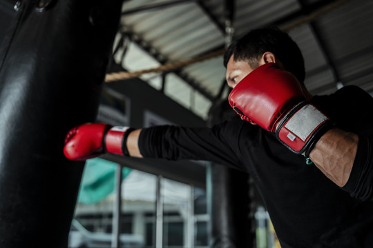 亚泰体育男子戴红手套打孔沙袋。在体育馆练习泰拳。