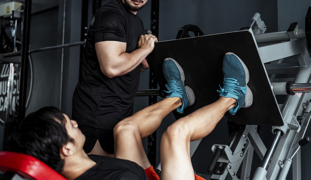 教练帮助会员健身房锻炼腿部压力机。体育精神。