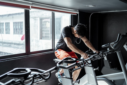 运动员亚泰体育男子穿着橙色裤子在健身房的自行车上锻炼。