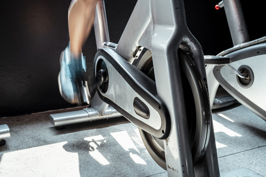 特写一个男人在健身房的自行车健身机上锻炼的模糊腿。
