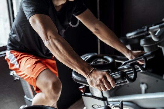 运动员亚泰体育男子穿着橙色裤子在健身房的自行车上锻炼。