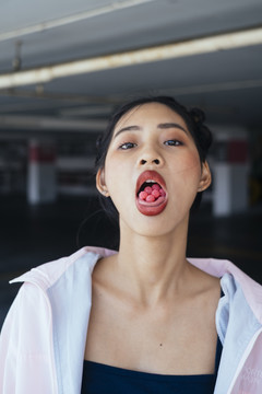 特写写真-年轻迷人的亚泰女性深色双髻发型，粉色头巾，嘴里塞满棒棒糖。