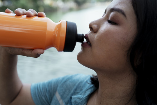 特写口渴的胖乎乎的亚洲女人从橘子瓶子里喝水。