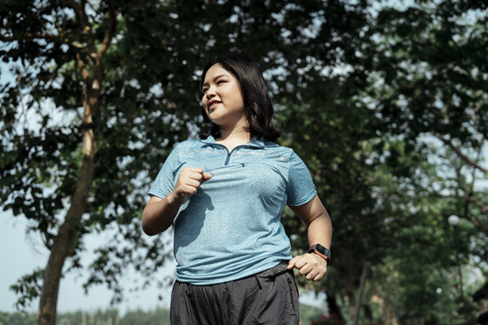 胖乎乎的运动型亚洲女人穿着蓝色运动服在公园跑步和慢跑。