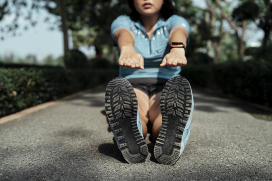 胖乎乎的运动型亚洲女子，穿着蓝色运动服，在公园的跑道上伸展双腿。