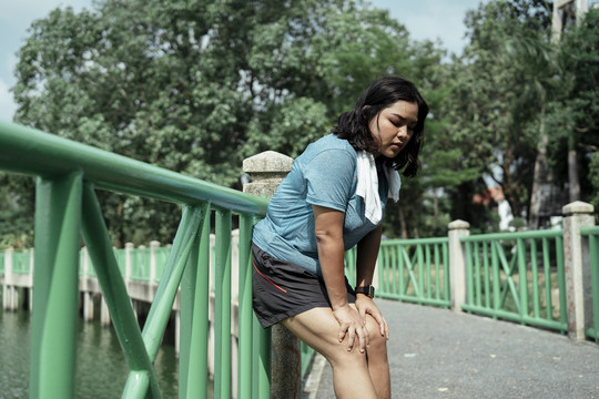 胖乎乎的运动型亚洲女性，穿着蓝色运动服，脖子上挂着白色毛巾，跑步后放松。