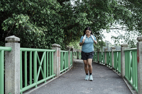 胖乎乎的运动型亚洲女人，穿着蓝色运动服，脖子上挂着白毛巾，在赛道上激情奔跑。