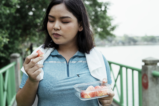 胖乎乎的运动型亚洲女人，穿着蓝色运动服，运动后吃苹果片。