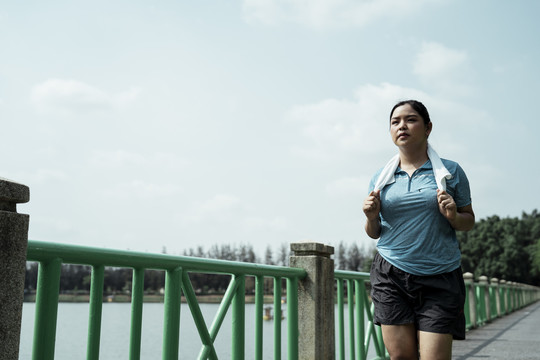 胖乎乎的运动型亚洲女性，穿着蓝色运动服，在大自然的跑道上奔跑。