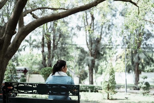 后视图-胖乎乎的运动型亚洲女子穿着蓝色运动服在公园的长凳上休息。