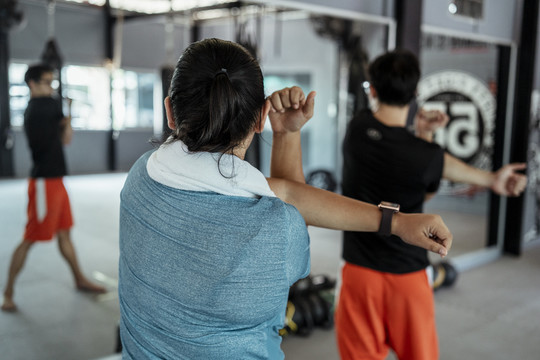 胖乎乎的运动型亚洲女性，穿着蓝色运动服，在健身房锻炼前和教练一起伸展。