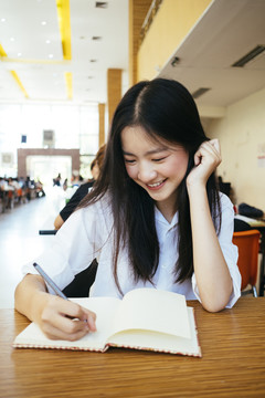 漂亮的黑发青年大学生在图书馆用钢笔在书页上统一书写。