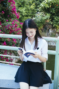 美丽的黑发青年大学生身着校服在花园户外看书。