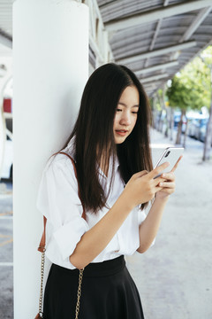 漂亮的深色长发年轻大学生身着制服在智能手机上发短信聊天。