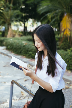 美丽的黑发青年大学生身着校服在户外看书。
