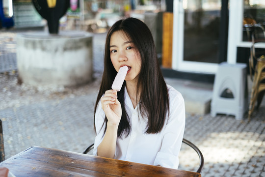 美丽的深色长发年轻大学生身着校服，喜欢在夏天吃冰激凌棒。