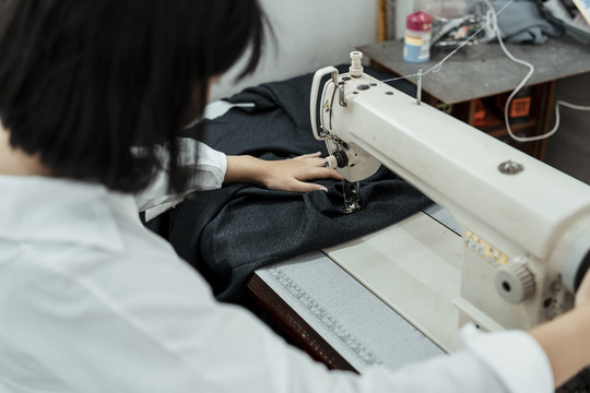 年轻的泰国女设计师在黑布上使用缝纫机。