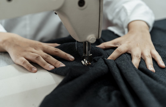 在工作台用缝纫机在黑布上工作的妇女的手。