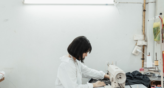 侧视图年轻的泰国设计师妇女在缝纫机站工作在白色的房间。