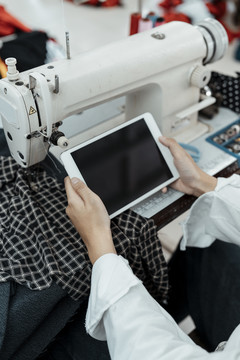 设计师的手在缝纫站的桌子上用平板电脑寻找更多关于衣服的信息细节。