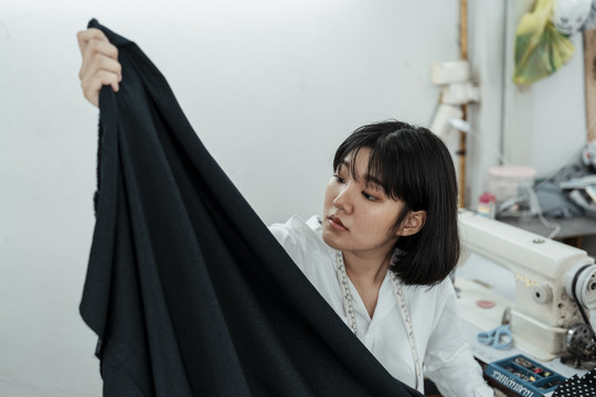 年轻的亚洲设计师在缝纫机站挑选布料做衣服。