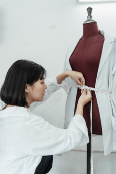 年轻的亚洲设计师用卷尺在假人腰部制作西装。