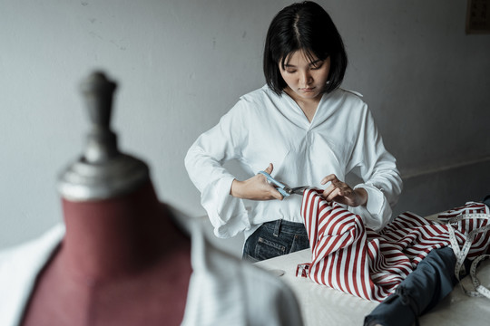 年轻的亚洲设计师在展厅里用剪刀裁布做衣服。