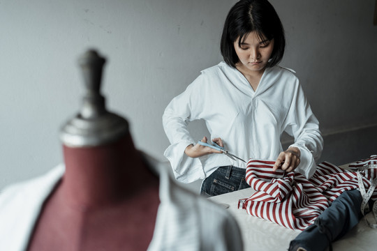 年轻的亚洲设计师在展厅里用剪刀裁布做衣服。