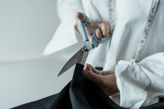 复制空间-年轻的亚洲设计师在服装制作过程中使用剪刀切割原布。
